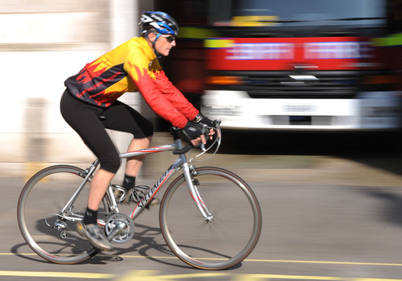 Man riding on a bicycle past a fire engine 