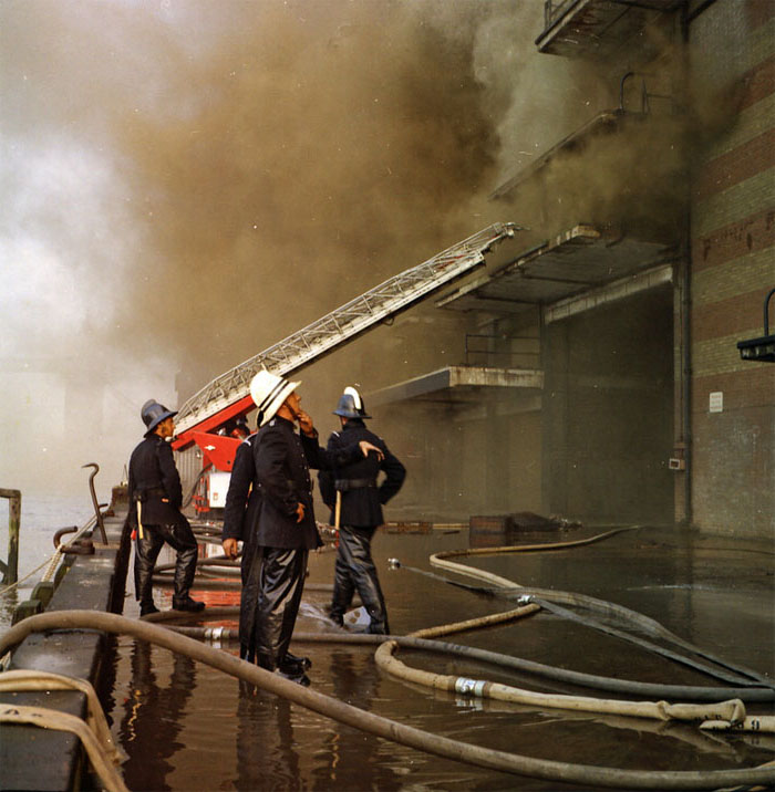 A photo of four firefighters looking up at Wilson's Wharf with lots of smoke around them
