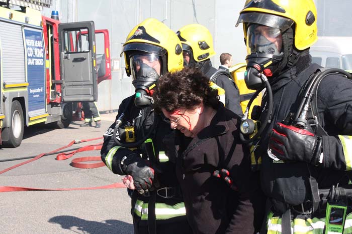 two firefighters are holding a woman up as she bleeds from the head in organised training exercise 