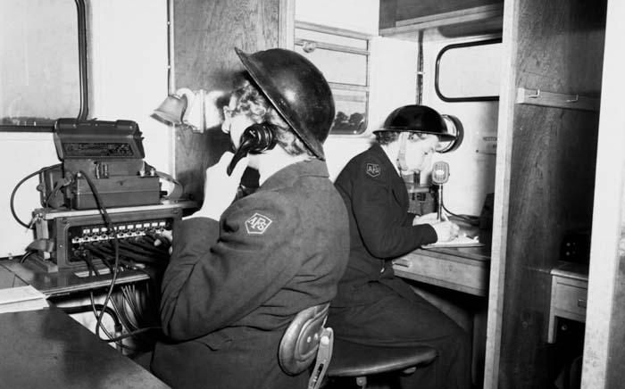 Black and white photograph of two female firefighters both wearing helmets answering phones 