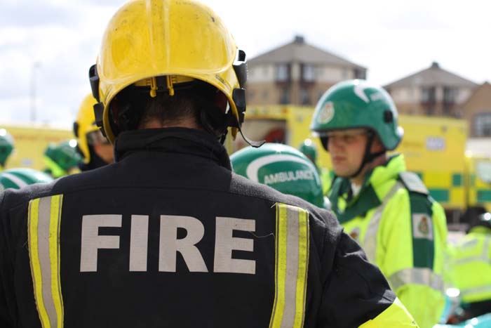 Firefighter with his back to the camera, ambulance service staff slightly blurred in the background