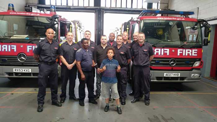 Group of firefighters stood in front of two fire engines with a man they rescued and his carer 