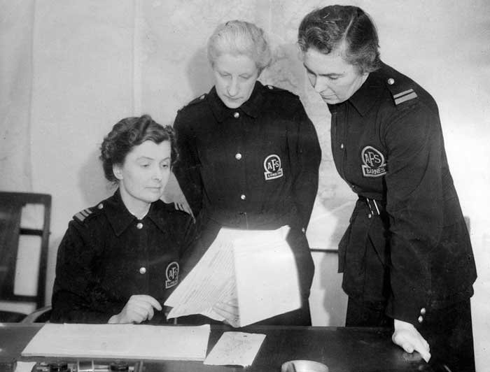 Black and white photograph of three female firefighters in uniform looking at a number of sheets of paper
