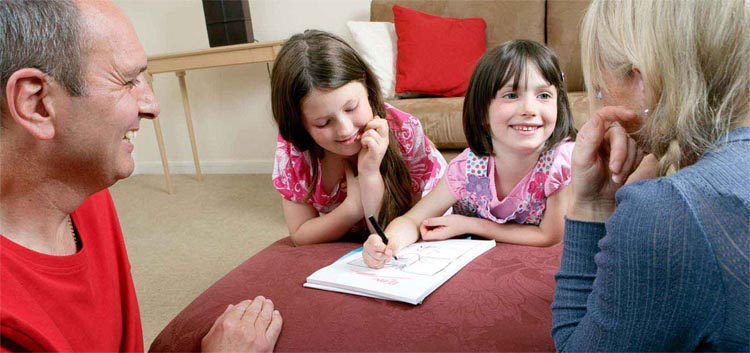Two young girls drawing while smiling at family members