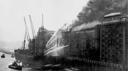 Historical photo of Firefighters using their fire hoses and a ship to put out fire in Butler Wharf 