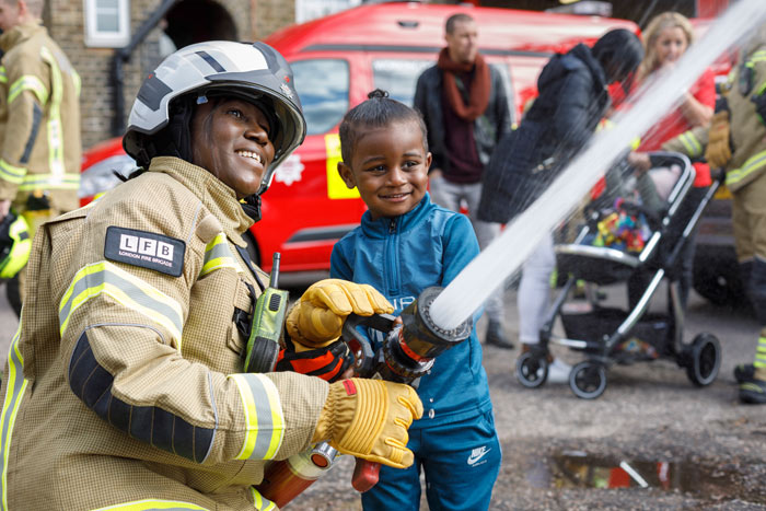 Firefighter helping a small child hold a hose.