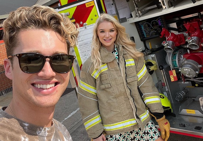 AJ Pritchard and Abbie Quinnen in front of a fire engine. Abbie wears a London Fire Brigade tunic.