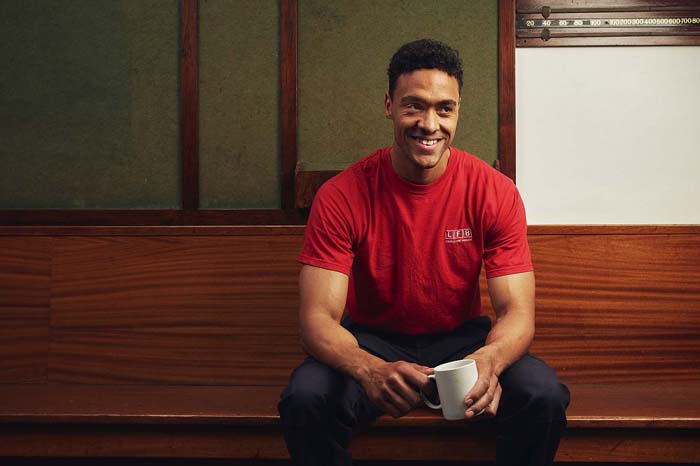 Firefighter sitting on a wooden bench holding a white mug and smiling.