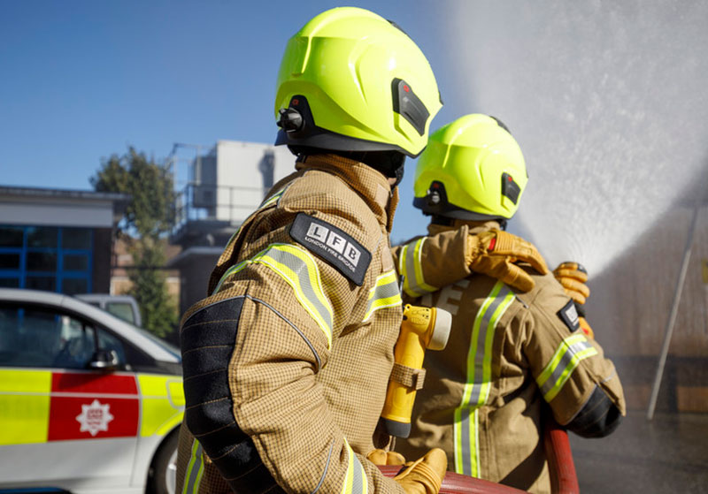 Two firefighters in gold PPE directing a hose.