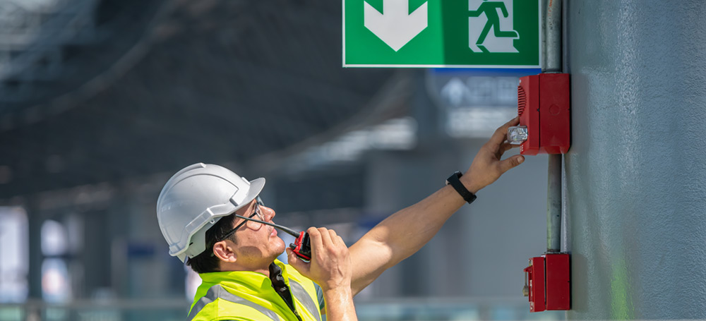 A man in a hard hat checking an automatic fire alarm system.