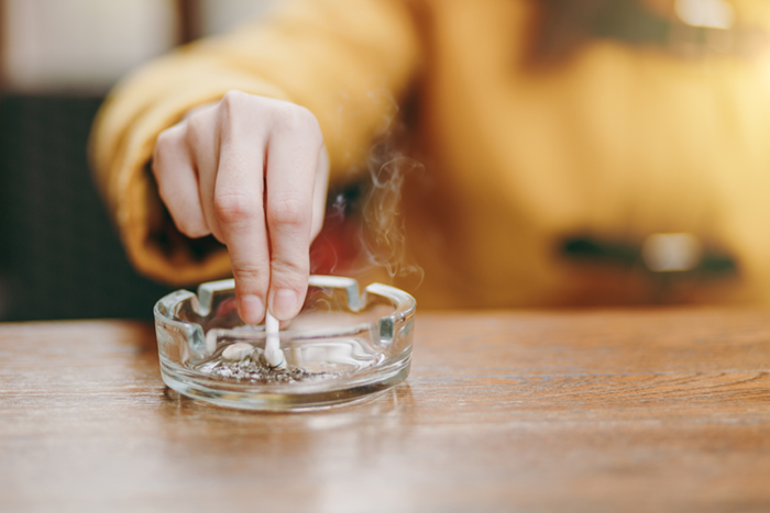 A hand stubbing out a cigarette in a heavy glass ashtray.