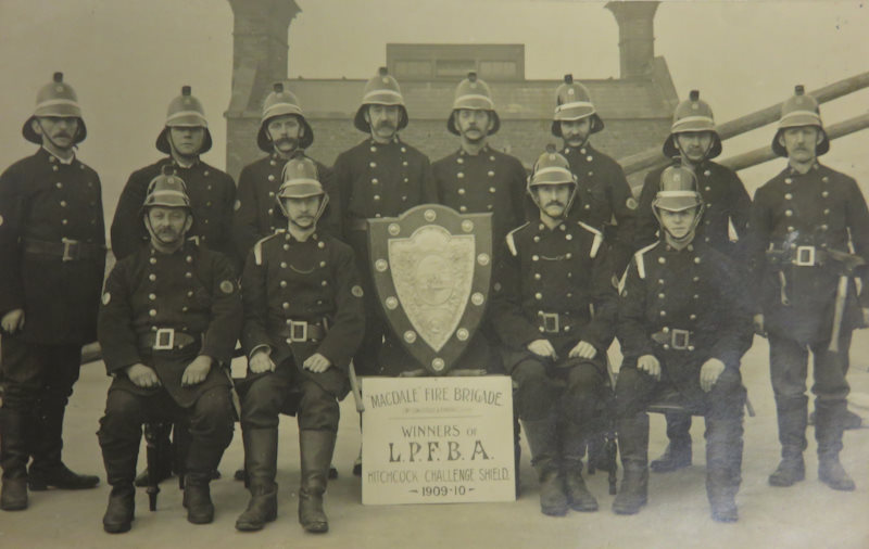 Firefighters from the private Macdale Fire Brigade posing with their plaque for winning London Private Fire Brigade Association in 1909-1910.