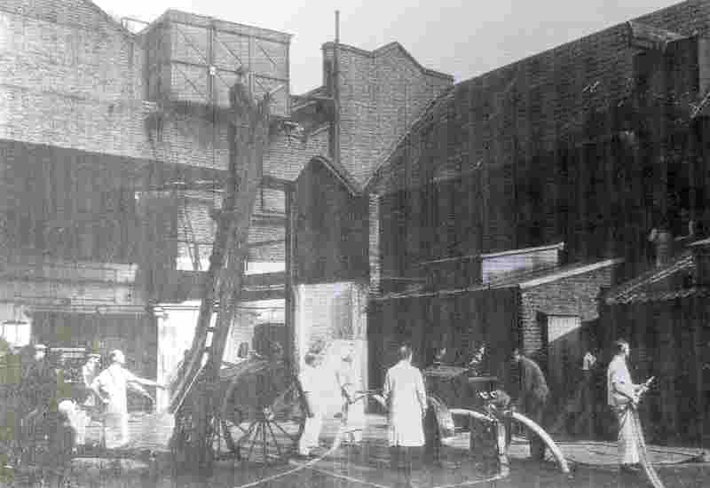 A Peek Frean Fire Brigade drill in 1935 using the wheeled escape ladder In 1935. The ladder is extended and members of the Brigade are standing around it, and using fire hoses to spray water towards a building.