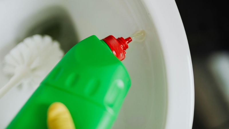 Stock image of a person pouring a bottle of bleach into a toilet bowl in order to clean it