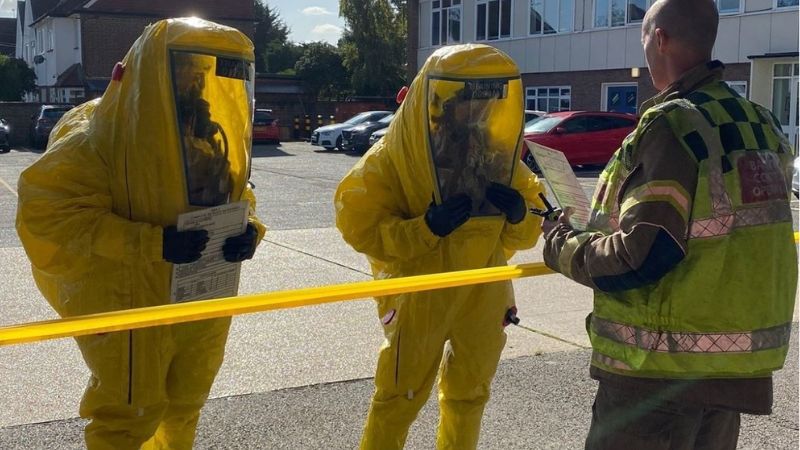 Two firefighters in yellow gas tight suits receive a briefing from an officer during a training exercise.