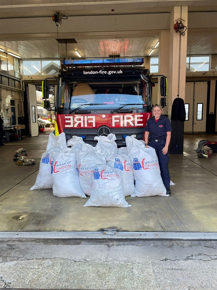 A firefighter poses in front of a fire engine with bags of donated coats