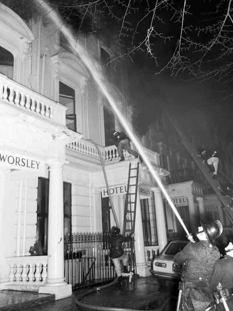 Exterior view of the Worsley Hotel in 1974 during a fire in the building. London Fire Brigade crews are attending the scene and directing water from hoses at the fire.